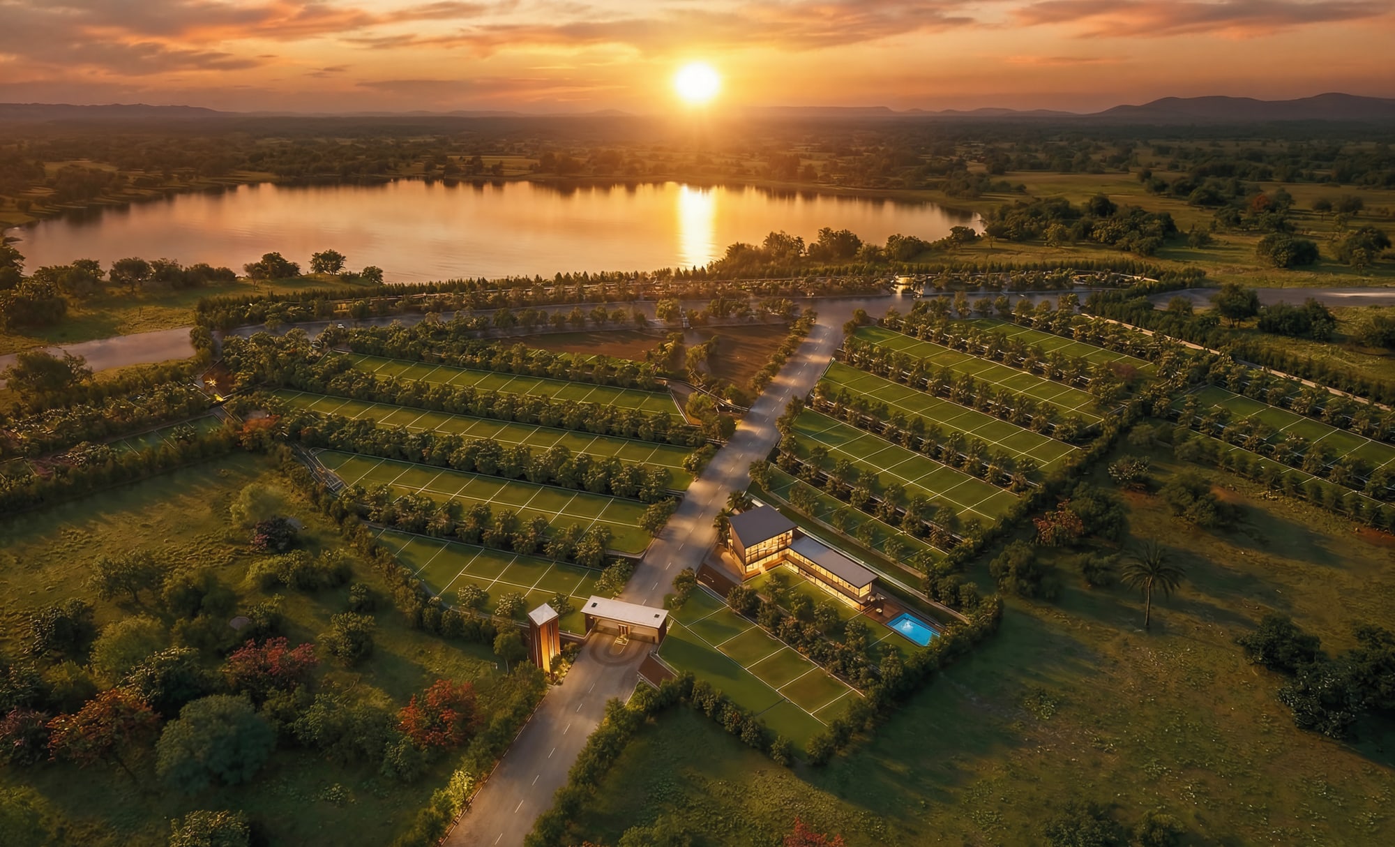 The estate at sunset: the entrance gate and clubhouse on the central avenue, plotted rows either side under mature trees, with open country and a lake beyond the boundary.